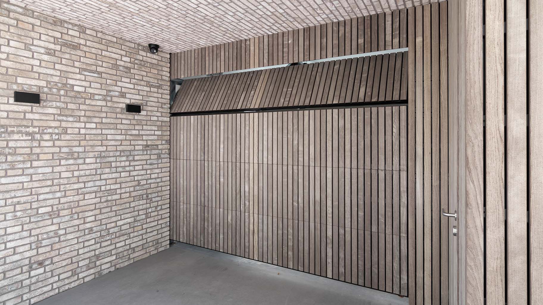 Onzichtbare houten garagedeur geïntegreerd in de gevel, gerealiseerd door Different Doors