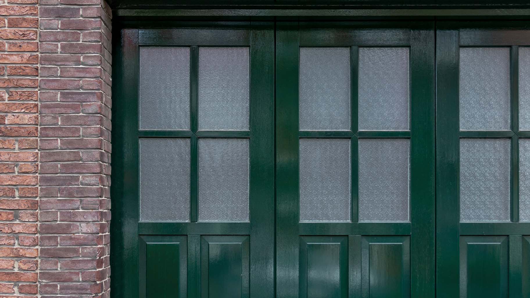 houten zijwaartse garagedeur met klassieke bossingpanelen en glas-in-loodramen