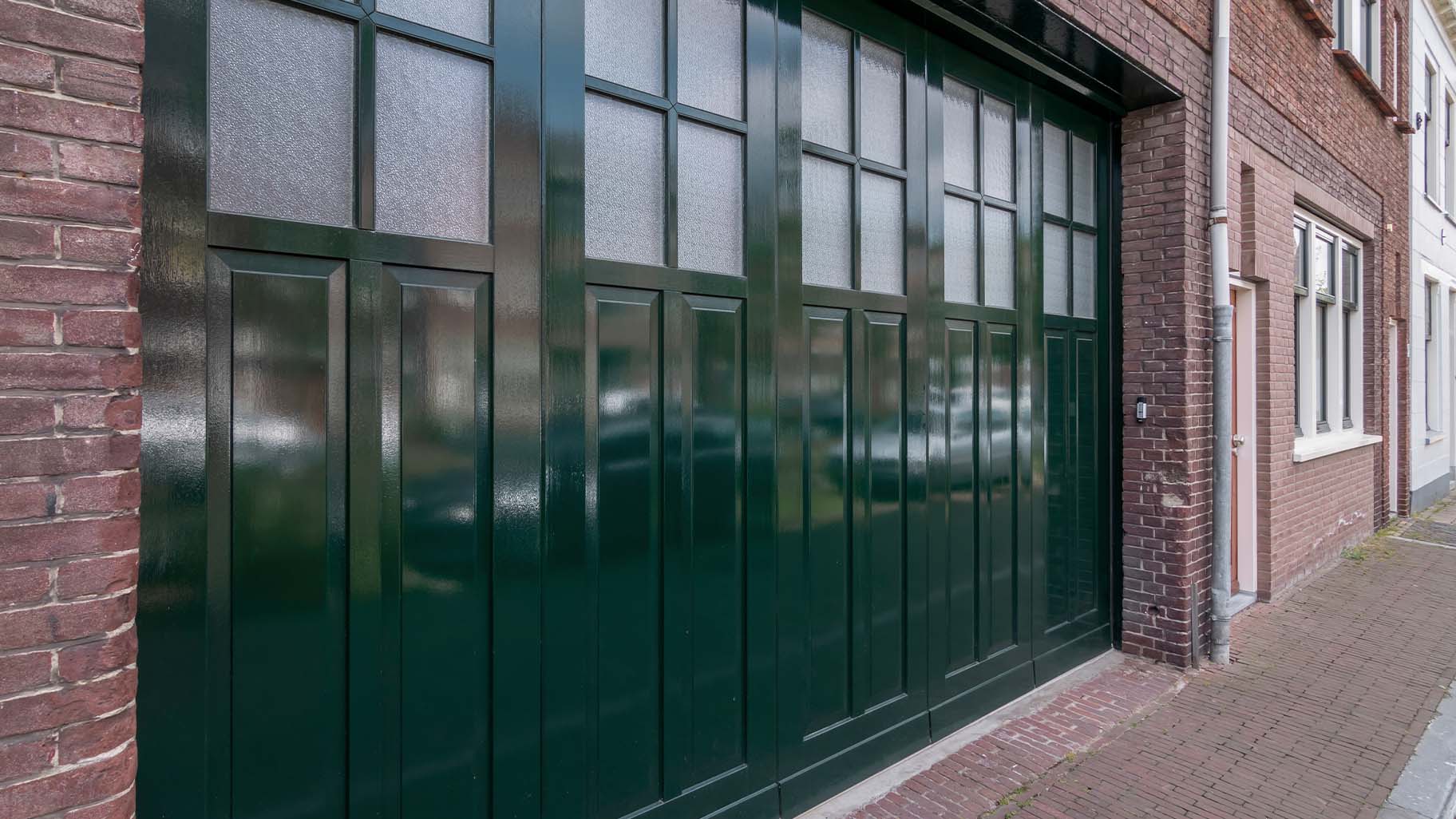 houten zijwaartse garagedeur met klassieke bossingpanelen en glas-in-loodramen