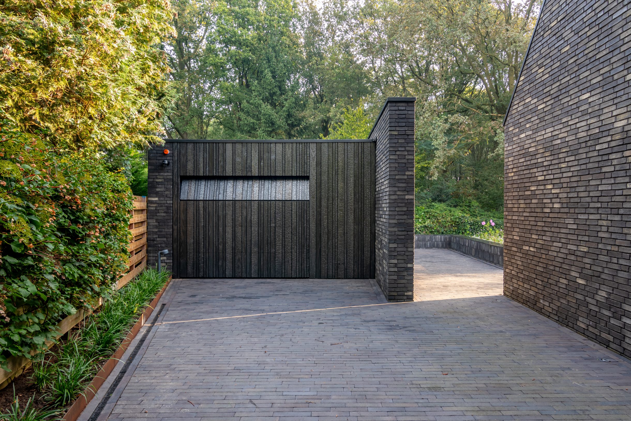 Moderne garage met Shou Sugi Ban garagedeur voor een minimalistische ontwerp