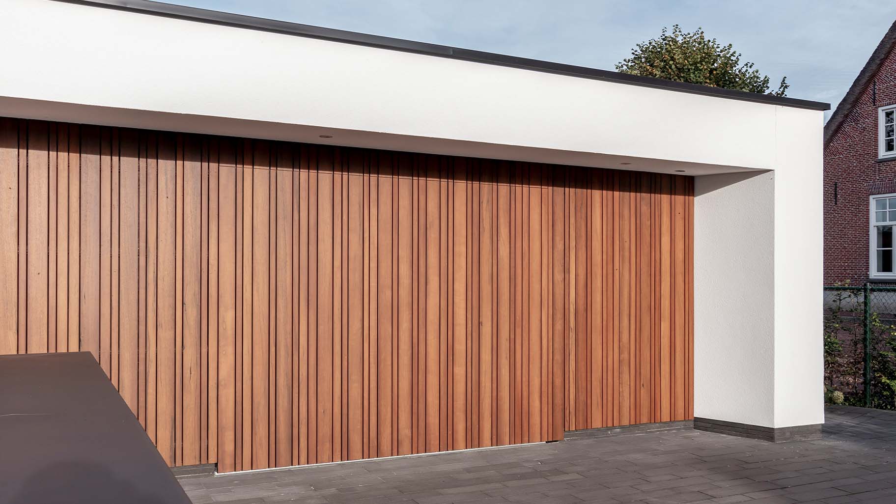 Zijwaartse fraké houten garagedeur die opgaat in de gevel, met strakke lijnen en uniforme uitstraling
