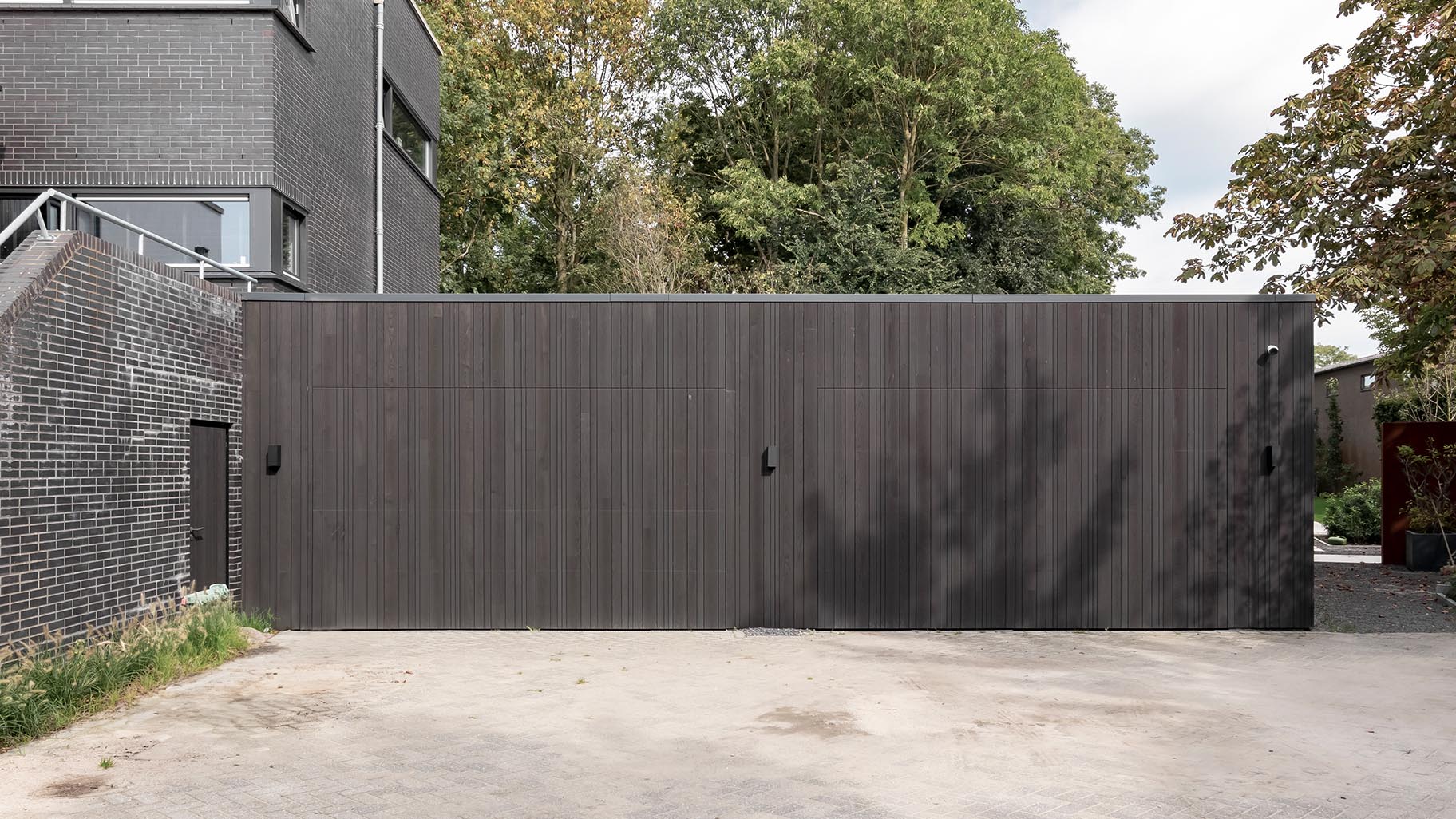 Donkere essenhouten garagedeuren verwerkt in de façade