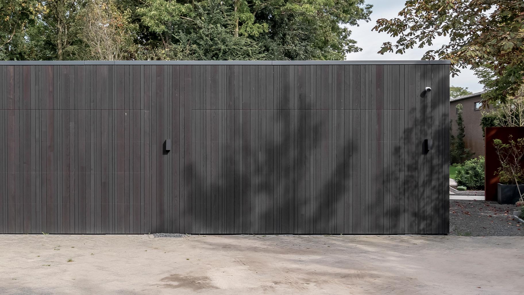 Donkere essenhouten garagedeuren verwerkt in de façade