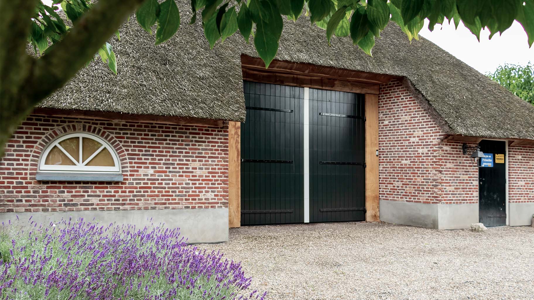Boerderij met rieten dak en houten sectionaal garagedeur, passend bij landelijke uitstraling