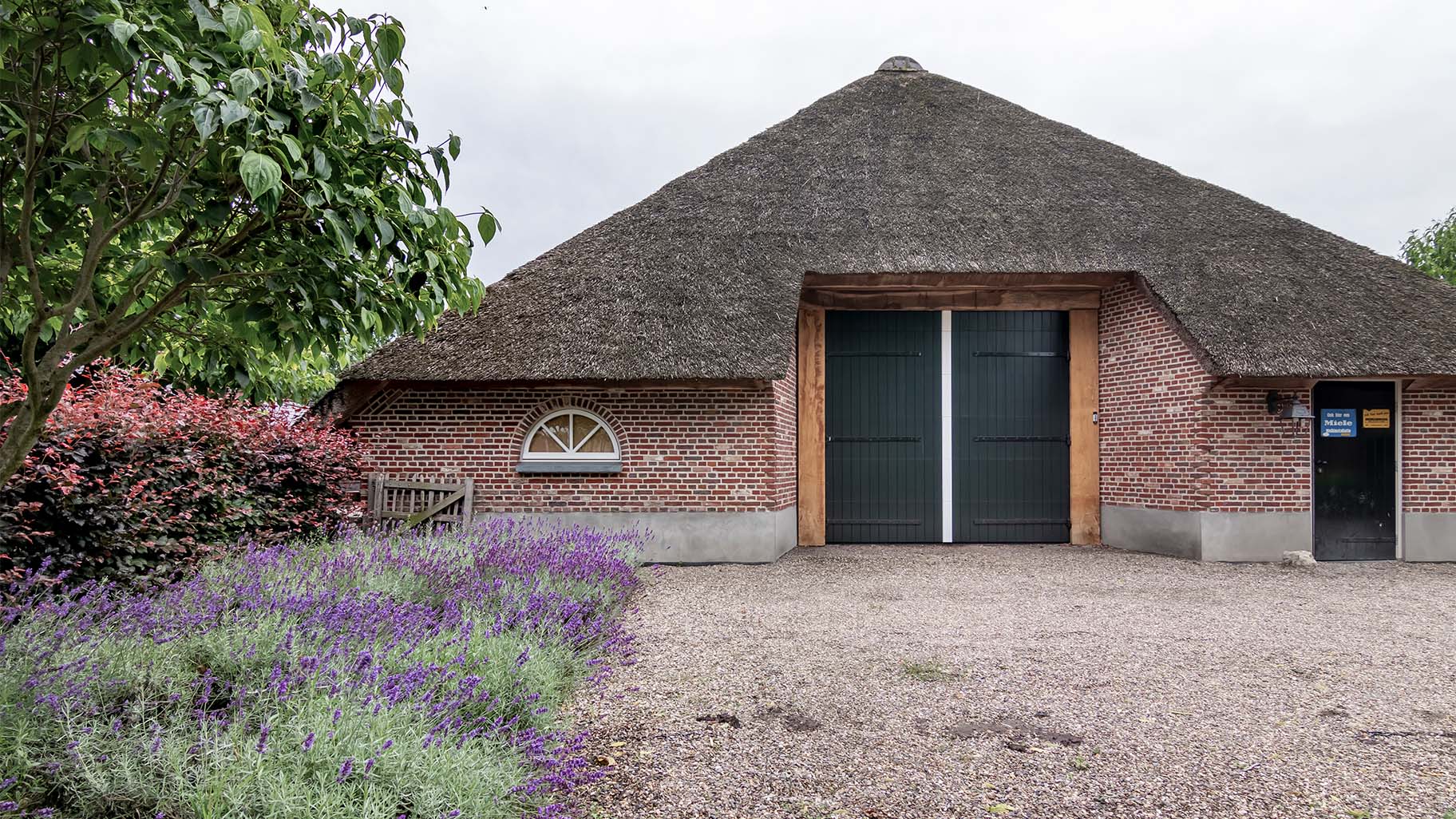 Boerderij met rieten dak en houten sectionaal garagedeur, passend bij landelijke uitstraling