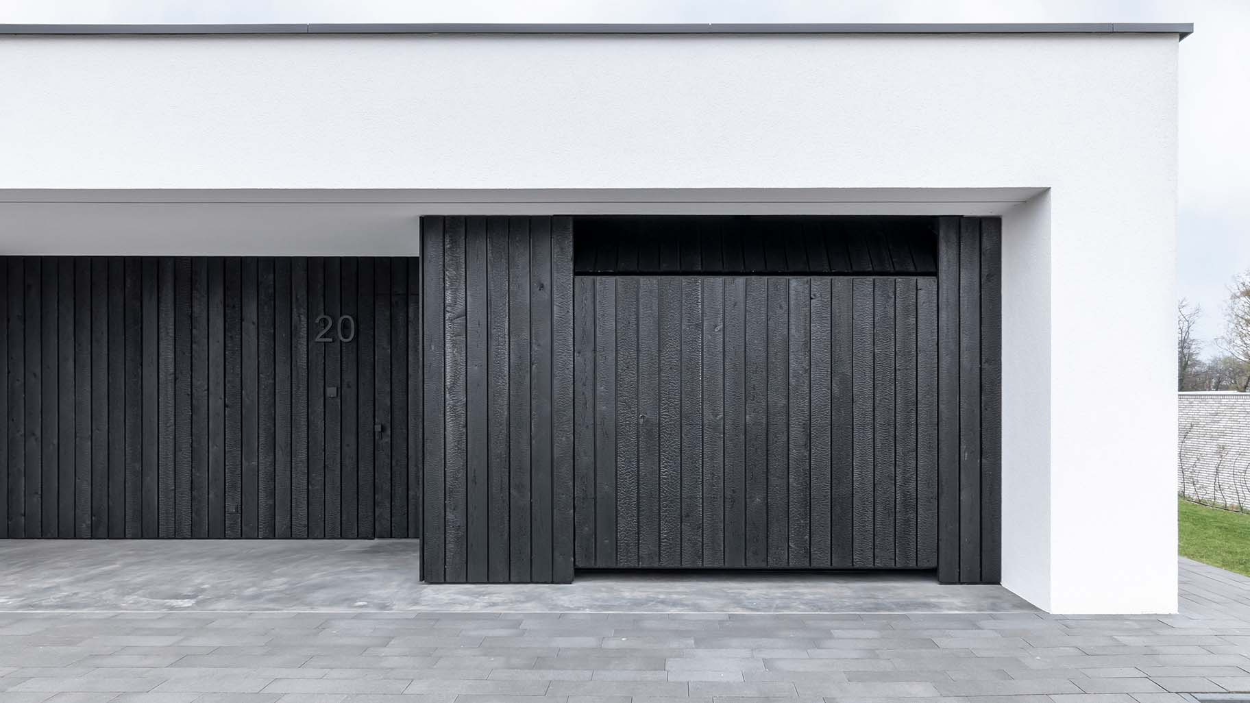Moderne woning met Shou Sugi Ban houten garagedeur en voordeur, gelijk met de zwarte gevel