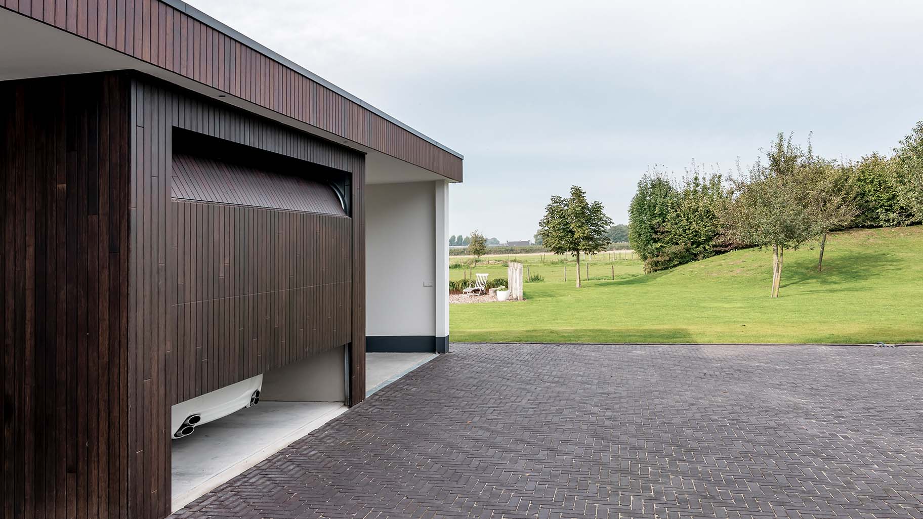 Carport met verticale sectionaaldeur van bamboe hout die een warme uitstraling