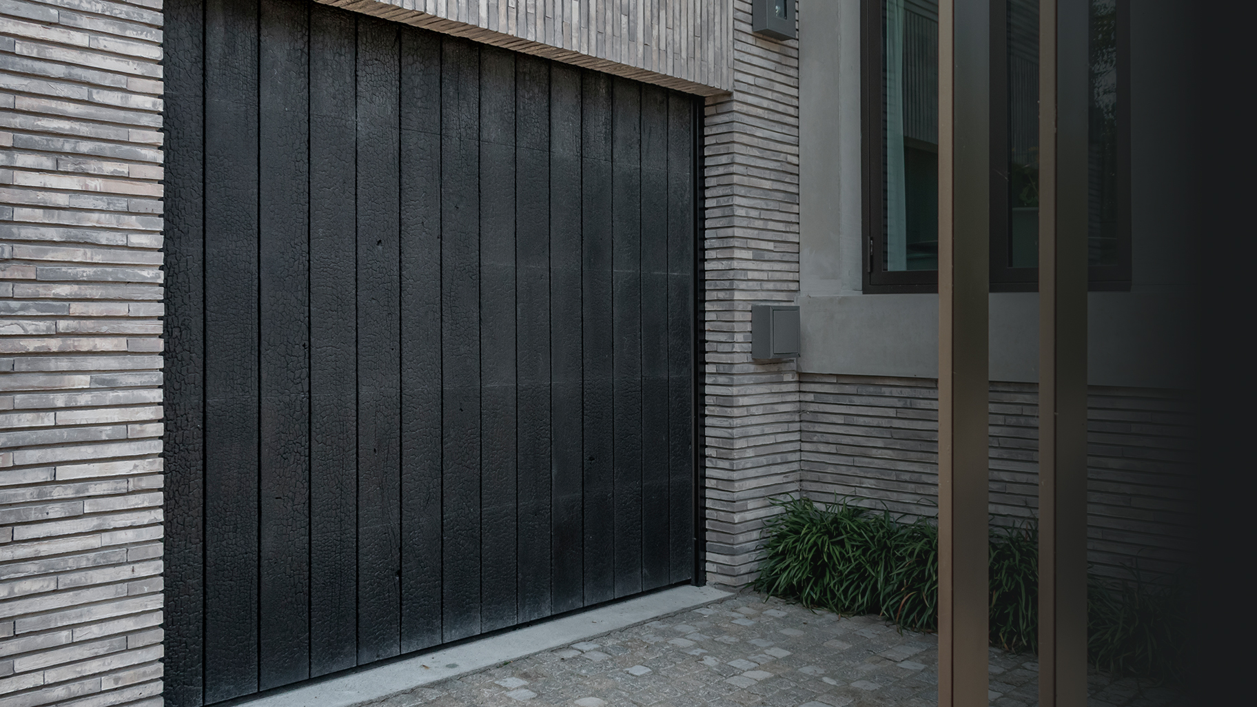 De Shou Sugi Ban garagedeur is achter de dag geplaatst, waardoor hij harmonieus opgaat in de gevel en de architectuur van de woning versterkt
