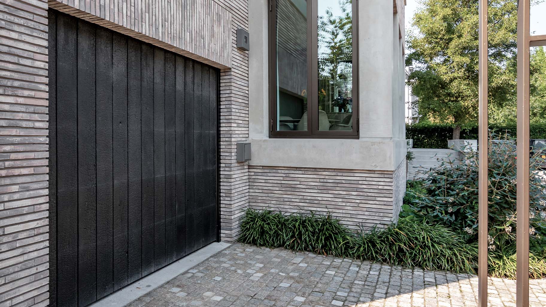 De Shou Sugi Ban garagedeur is achter de dag geplaatst, waardoor hij harmonieus opgaat in de gevel en de architectuur van de woning versterkt