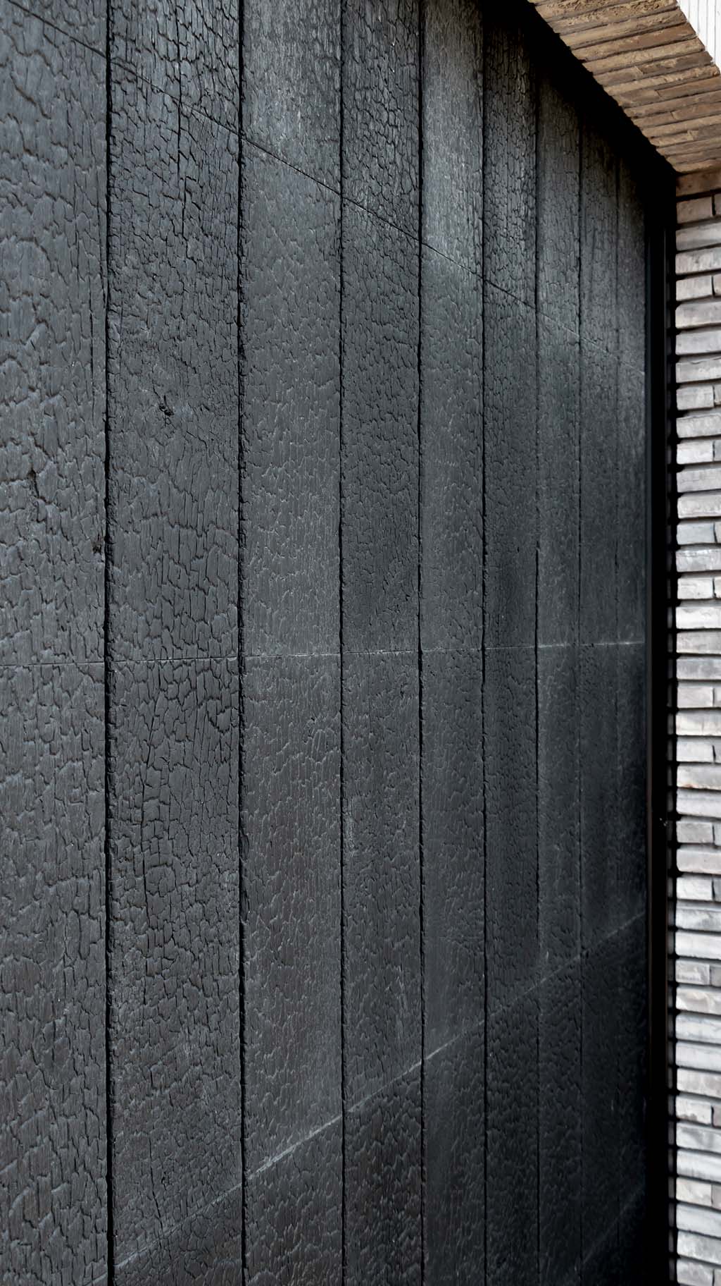 De Shou Sugi Ban garagedeur is achter de dag geplaatst, waardoor hij harmonieus opgaat in de gevel en de architectuur van de woning versterkt