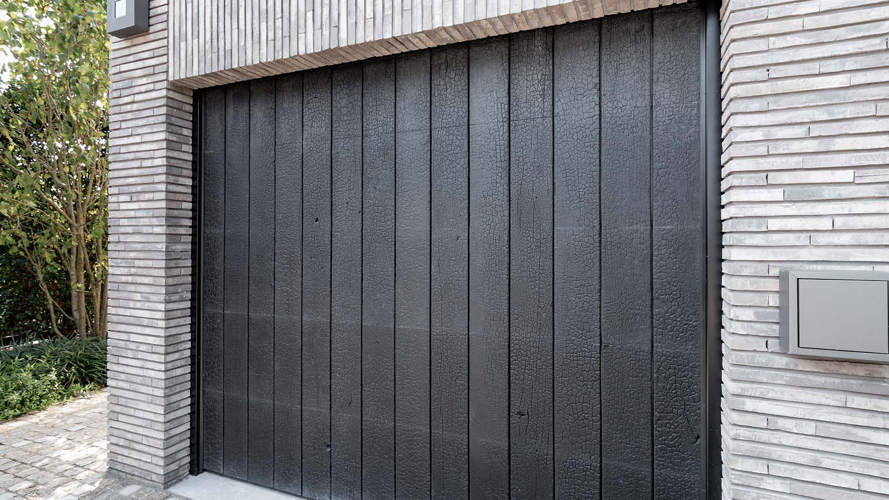 De Shou Sugi Ban garagedeur is achter de dag geplaatst, waardoor hij harmonieus opgaat in de gevel en de architectuur van de woning versterkt