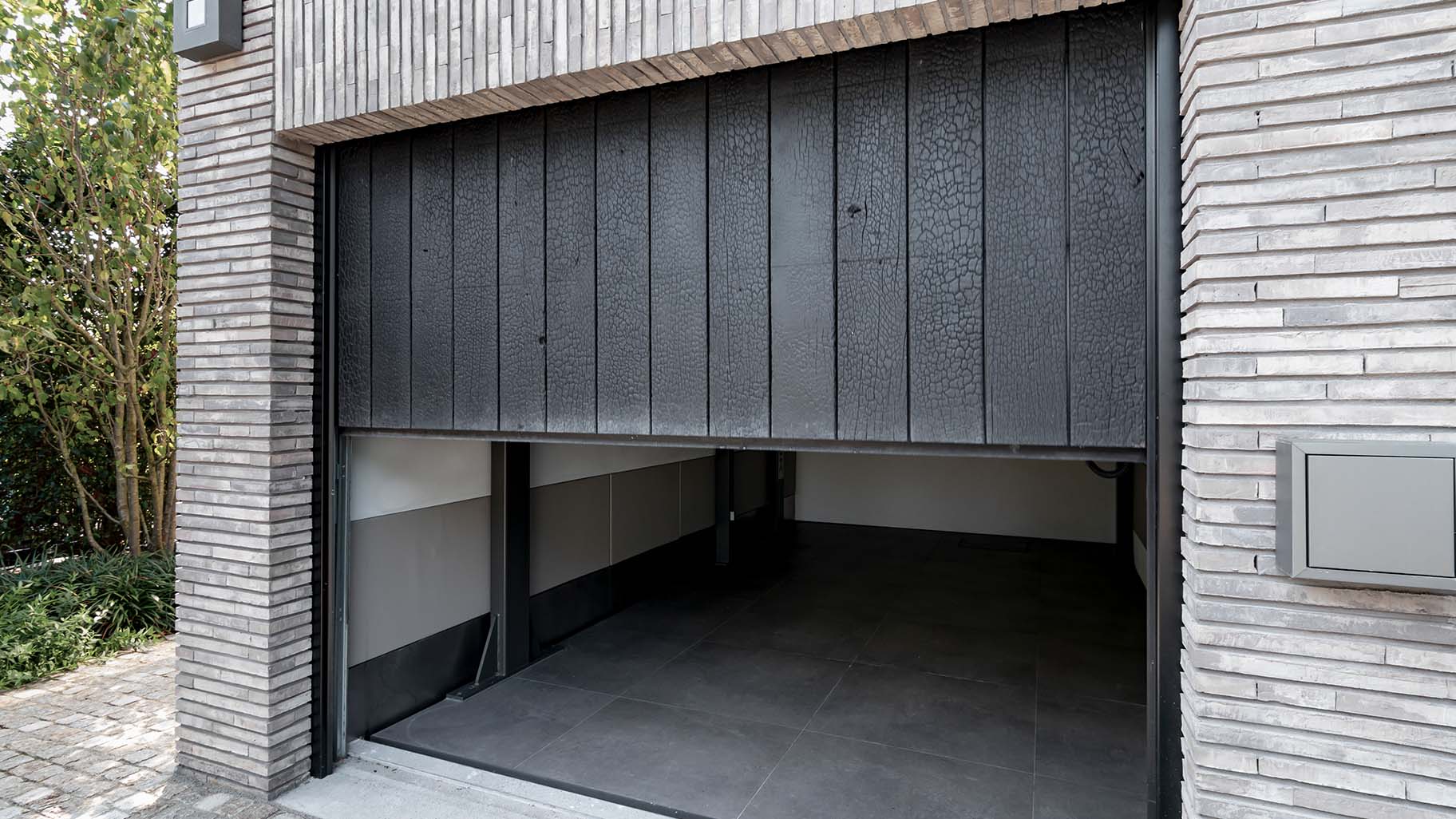 e Shou Sugi Ban garagedeur is achter de dag geplaatst, waardoor hij harmonieus opgaat in de gevel en de architectuur van de woning versterkt