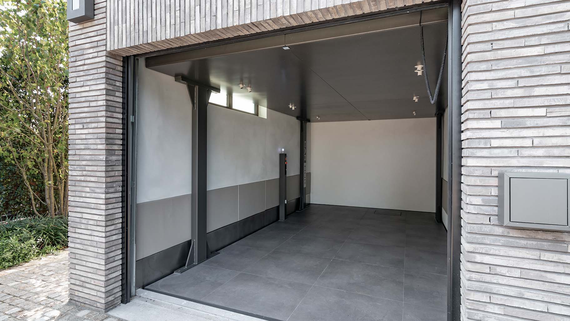 Shou Sugi Ban houten sectionaaldeur bij een moderne villa, die naadloos opgaat in de gevel en de krachtige uitstraling van de woning benadrukt