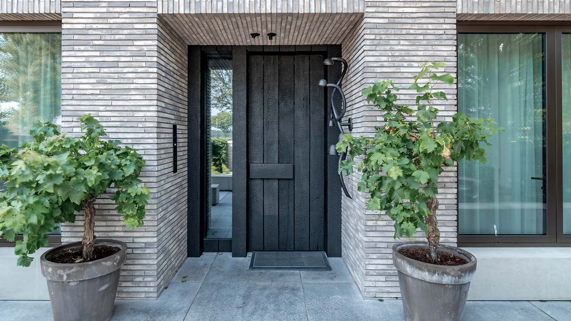 Shou Sugi Ban houten sectionaaldeur bij een moderne villa, die naadloos opgaat in de gevel en de krachtige uitstraling van de woning benadrukt