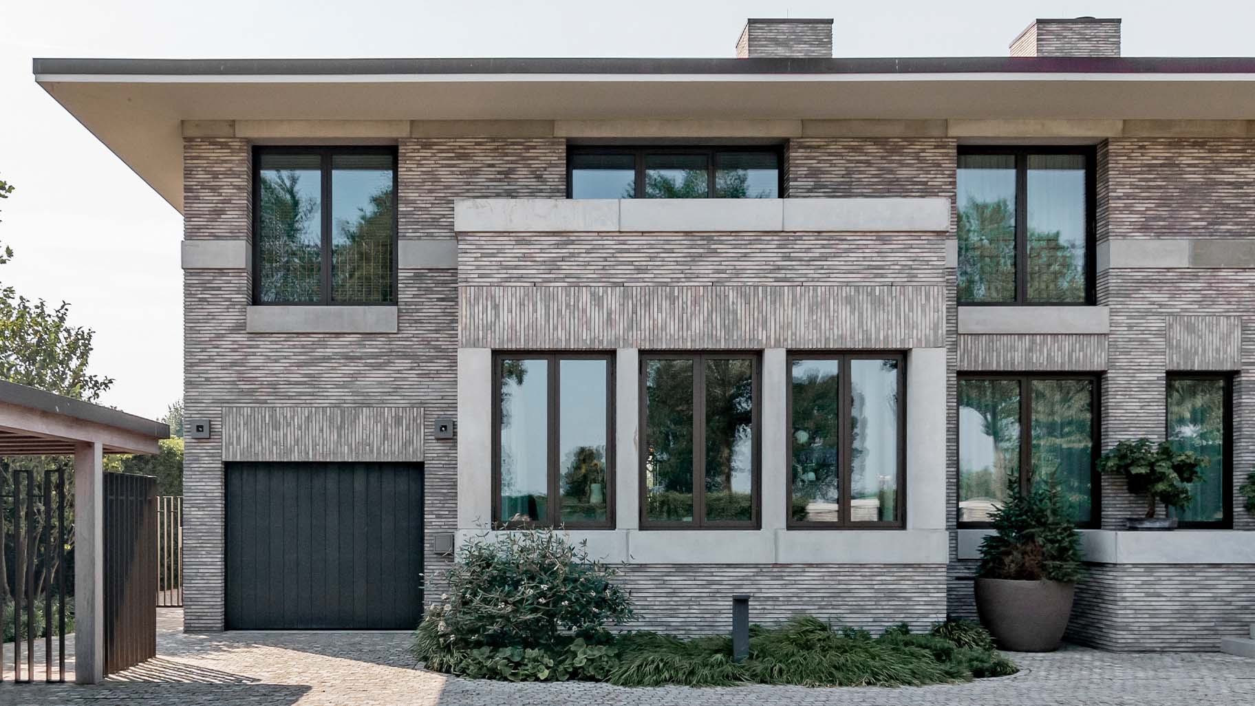 Shou Sugi Ban houten sectionaaldeur bij een moderne villa, die naadloos opgaat in de gevel en de krachtige uitstraling van de woning benadrukt