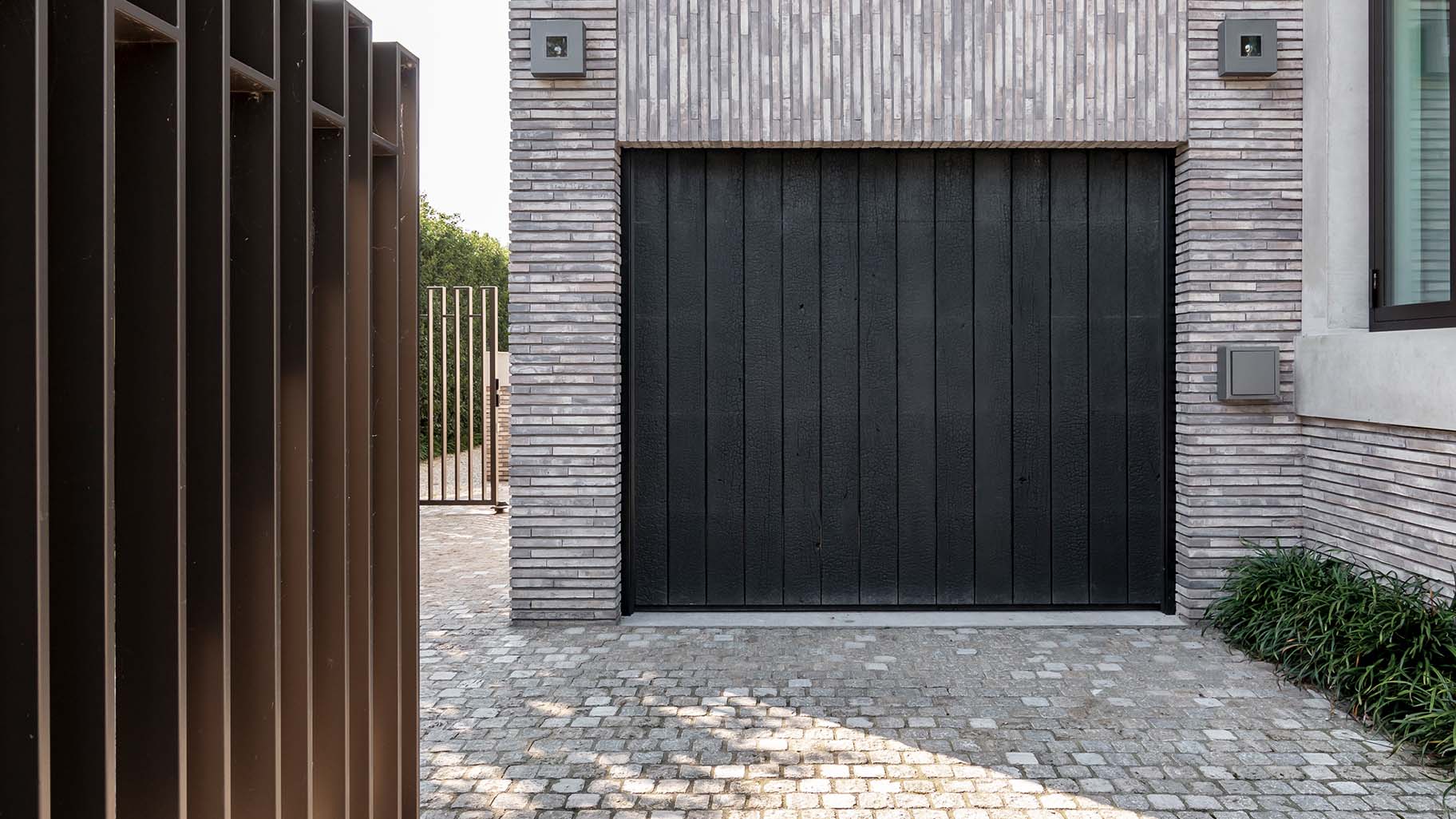 Moderne villa met een indrukwekkende Shou Sugi Ban houten garagedeur die achter de dag is geplaatst en perfect aansluit bij de strakke architectuur