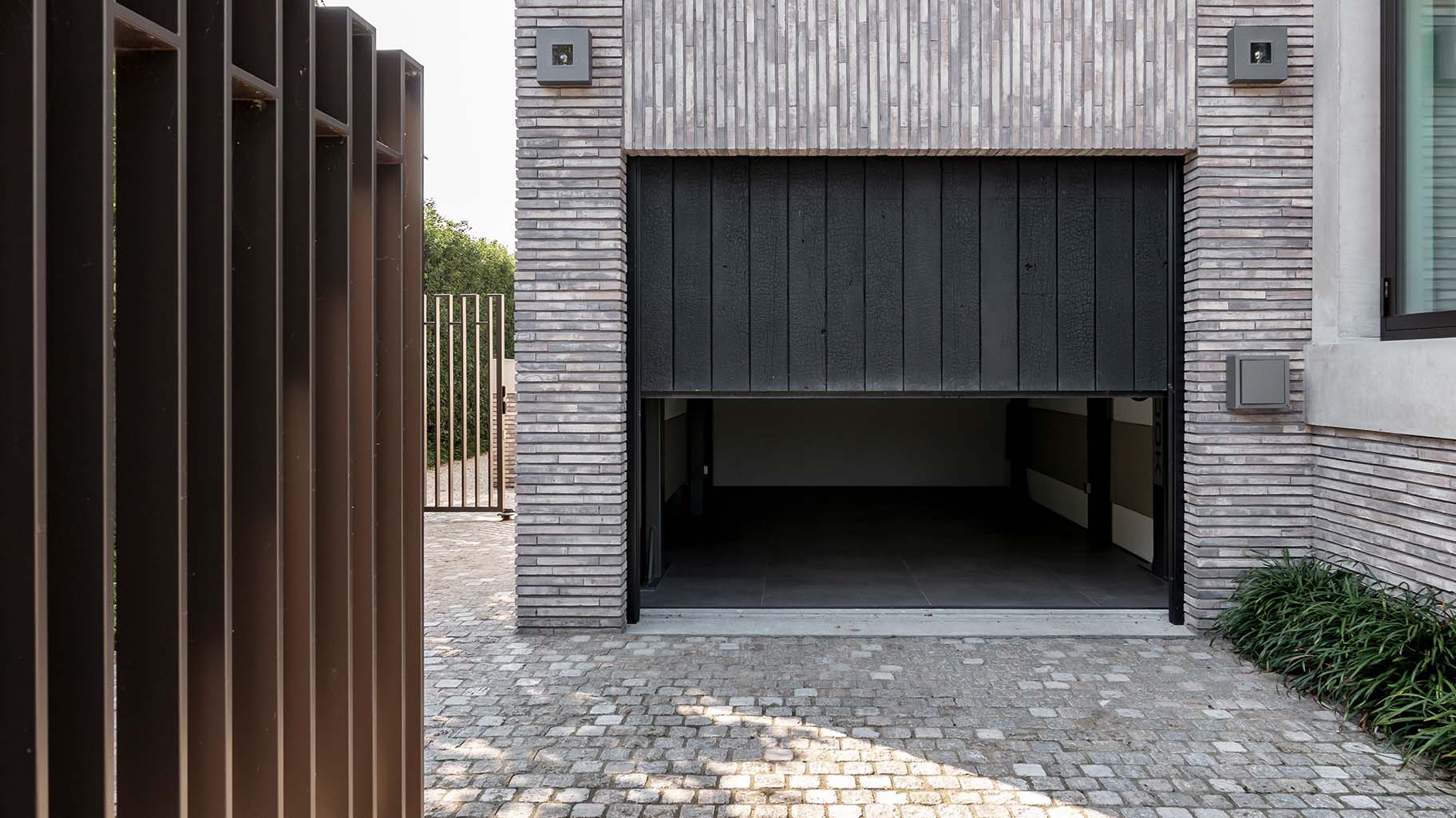 "Shou Sugi Ban houten sectionaaldeur bij een moderne villa, die naadloos opgaat in de gevel en de krachtige uitstraling van de woning benadrukt