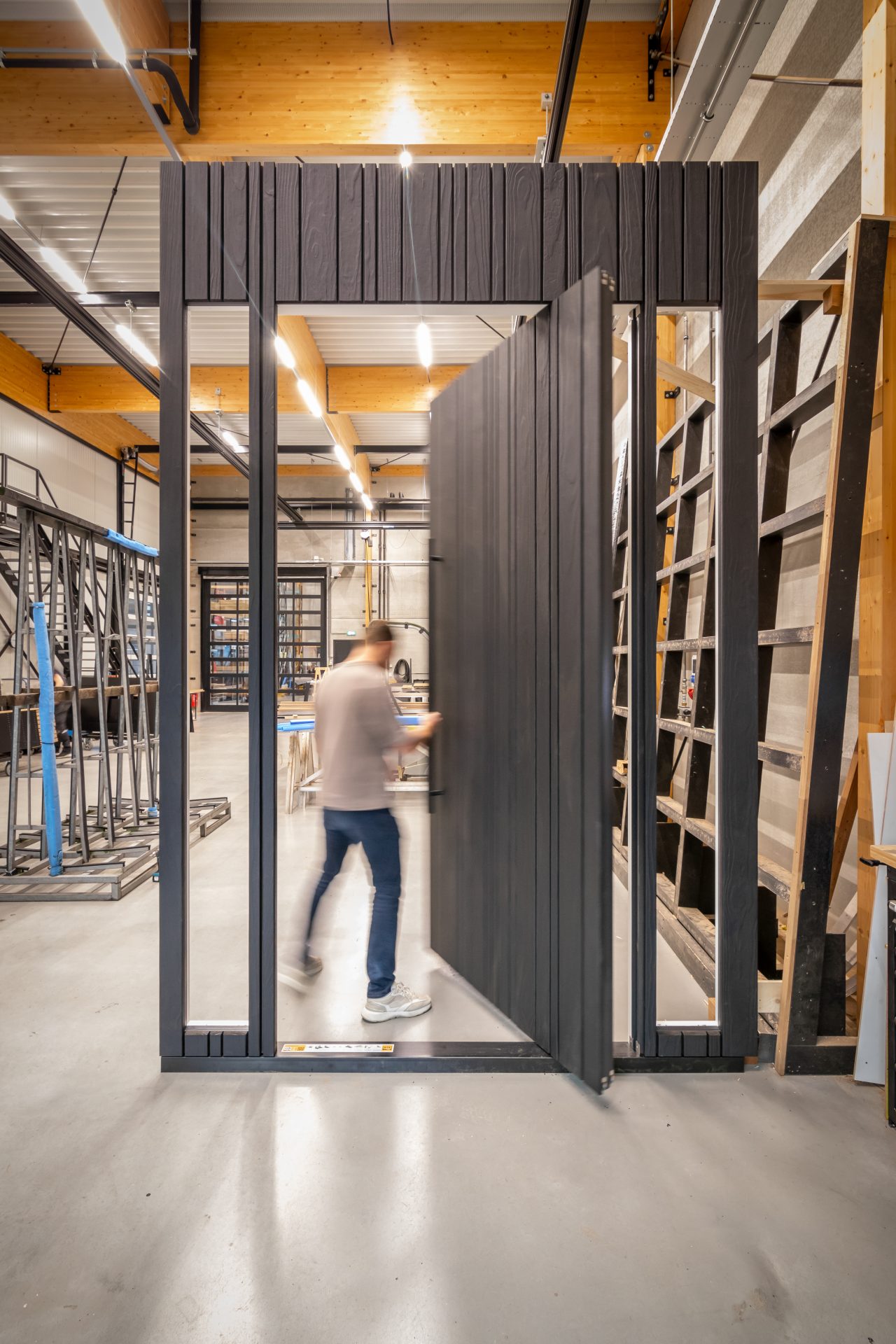 Een persoon opent de Shou Sugi Ban houten taatsdeur, die moeiteloos draait en naadloos opgaat in de gevel