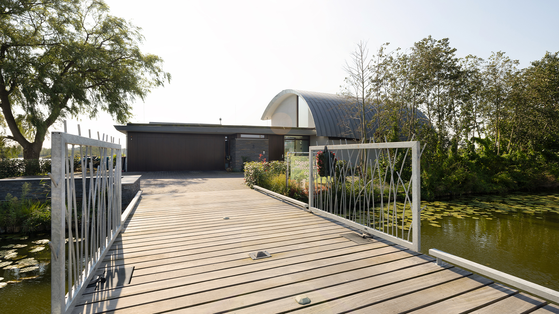 Onzichtbare zijwaartse garagedeur volledig gelijk is met de gevel geplaatst. Hierdoor lijkt de deur, wanneer gesloten, onzichtbaar en vormt deze een perfect doorlopende houten wand. De verticale houten latten geven de gevel een moderne, strakke uitstraling.