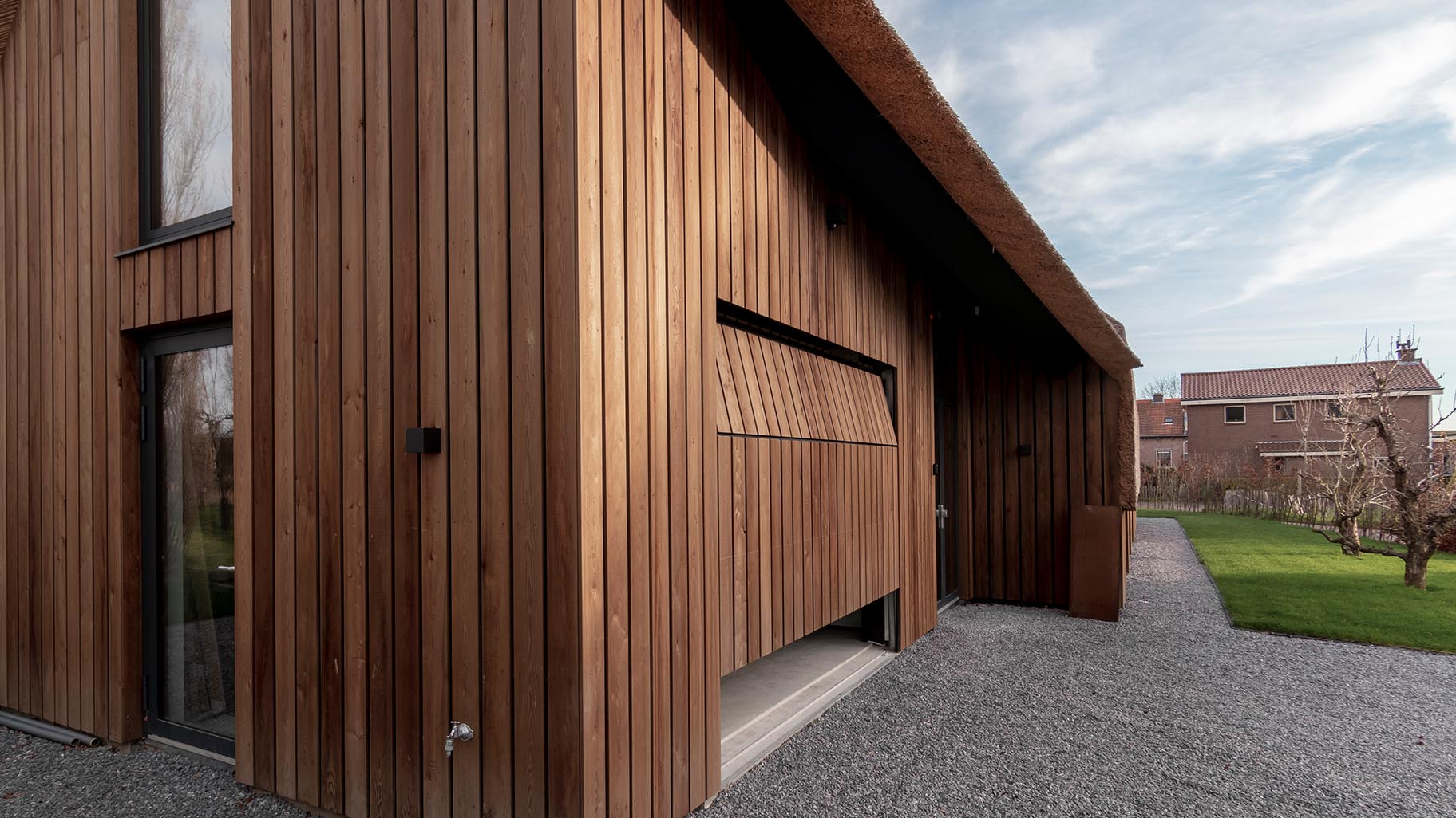 De houten garagedeur is gelijk met de gevel geplaatst, wat zorgt voor een onopvallende integratie in het ontwerp van de woning