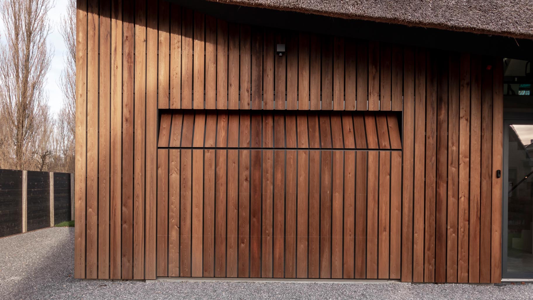 De houten garagedeur is gelijk met de gevel geplaatst, wat zorgt voor een onopvallende integratie in het ontwerp van de woning