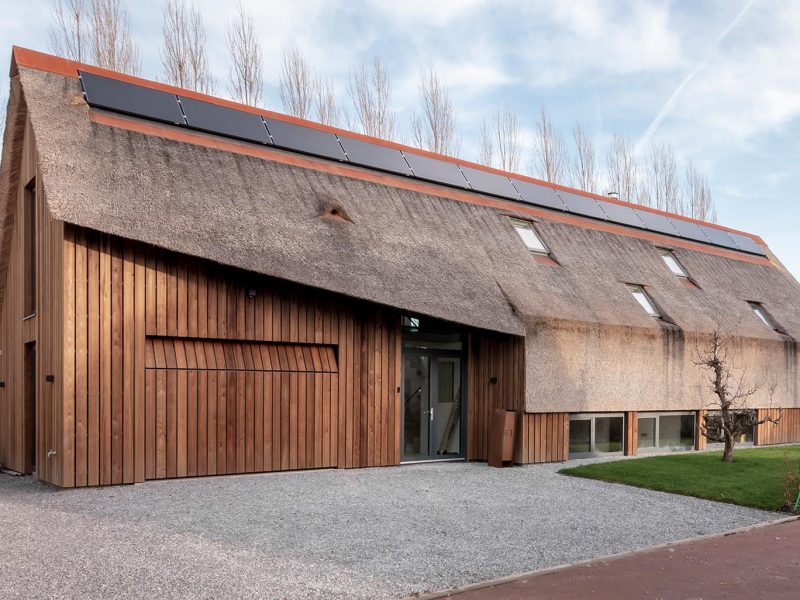 Moderne rietgedekte woning met een onopvallende verticale houten garagedeur die volledig opgaat in de gevel en verrast wanneer geopend