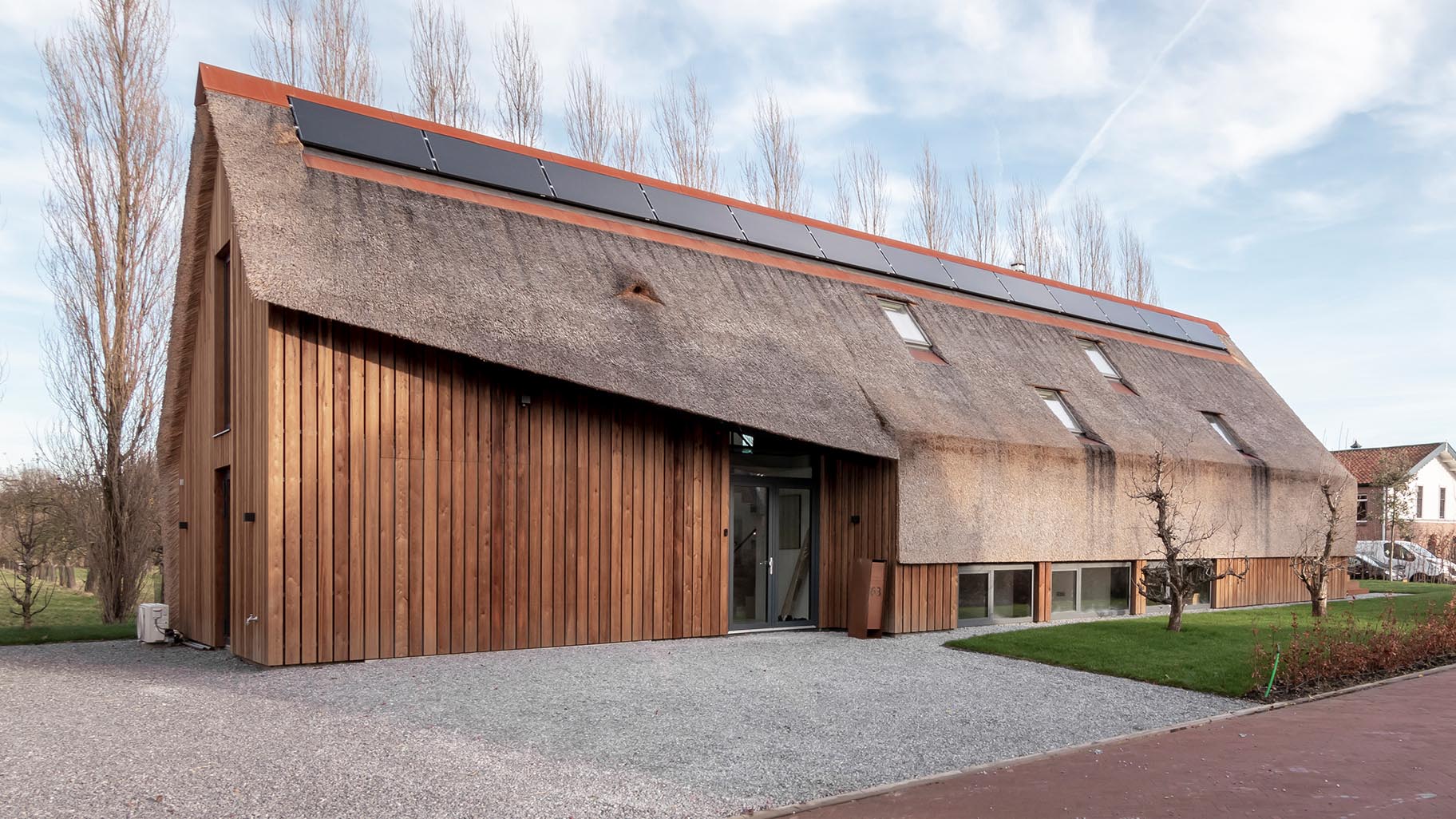 Moderne rietgedekte woning met een onopvallende verticale houten garagedeur die volledig opgaat in de gevel en verrast wanneer geopend