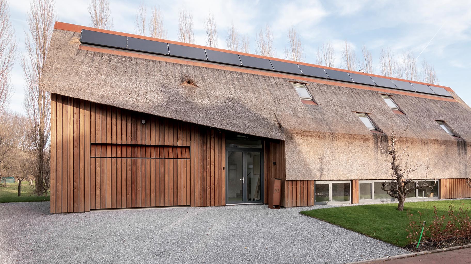 Moderne rietgedekte woning met een onopvallende verticale houten garagedeur die volledig opgaat in de gevel en verrast wanneer geopend