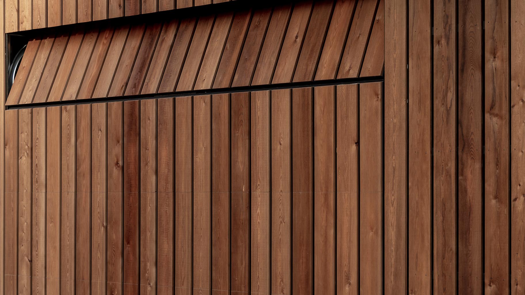 Verticale houten garagedeur geïntegreerd in de gevel, met natuurlijke houttinten