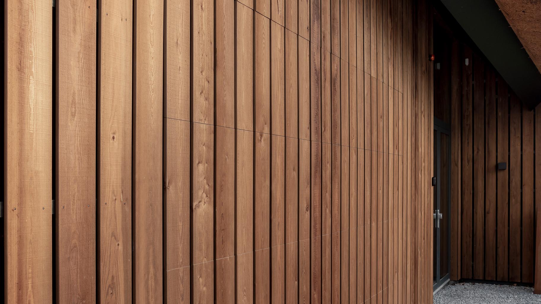 Verticale houten garagedeur geïntegreerd in de gevel, met natuurlijke houttinten
