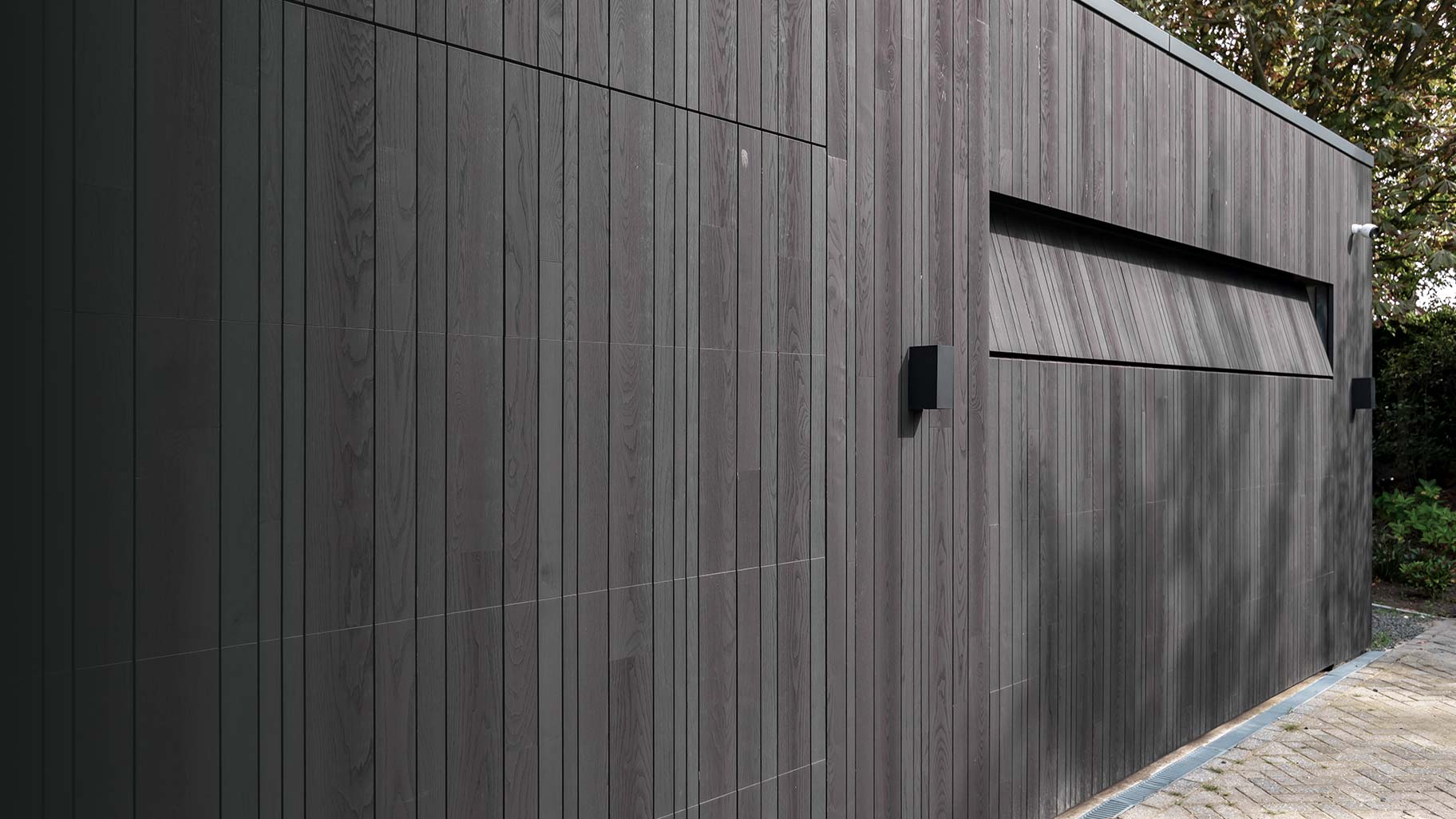 Donkere essenhouten garagedeuren verwerkt in de façade