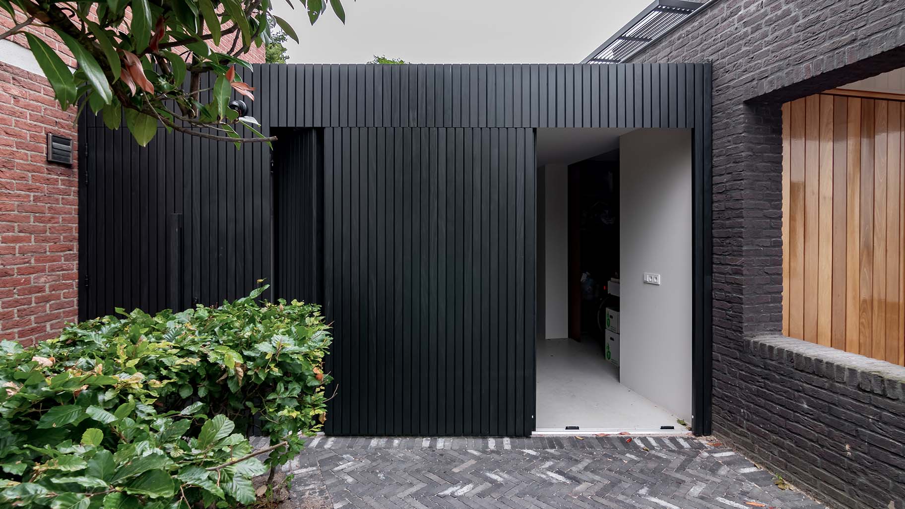 Op maat gemaakte zwarte houten zijwaartse garagedeur, gerealiseerd door Different Doors