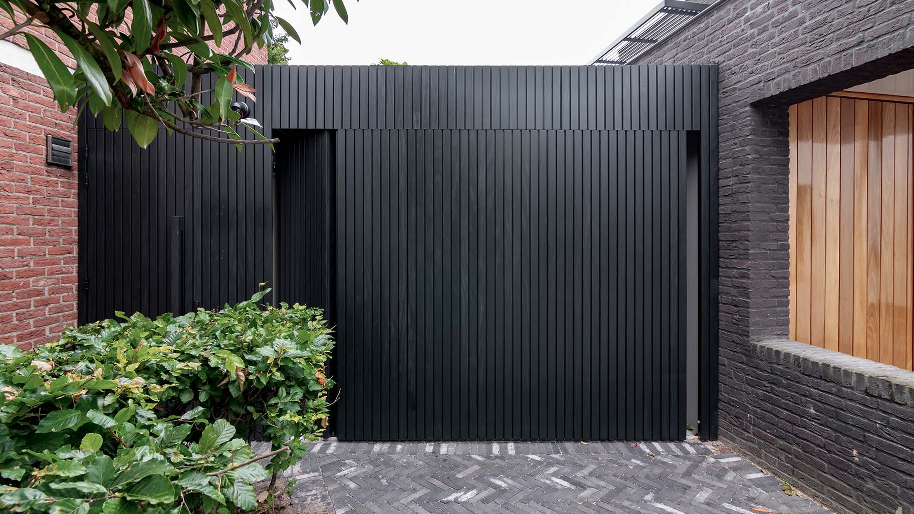 Op maat gemaakte zwarte houten zijwaartse garagedeur, gerealiseerd door Different Doors