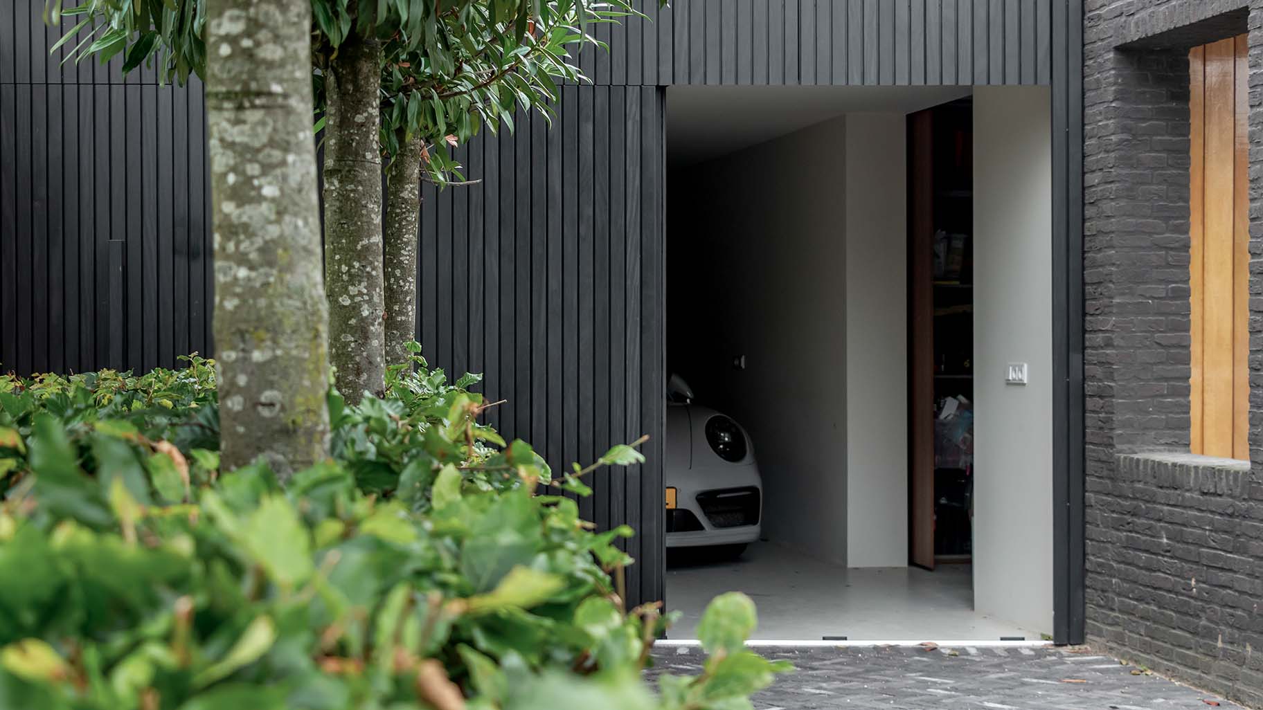 Moderne garage met een zwarte zijwaartse garagedeur van Afrormosia hout