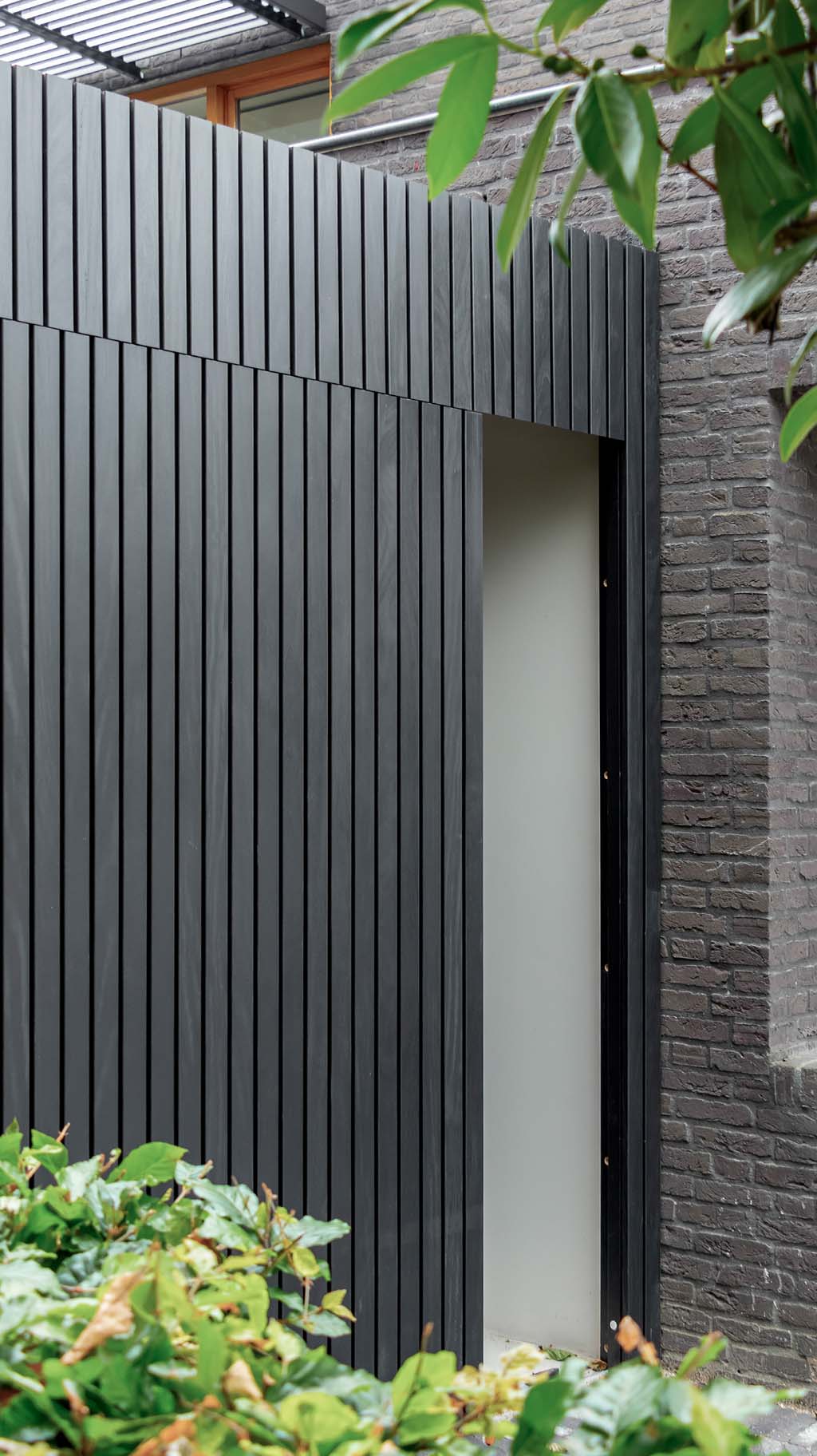 Moderne garage met een zwarte zijwaartse garagedeur van Afrormosia hout